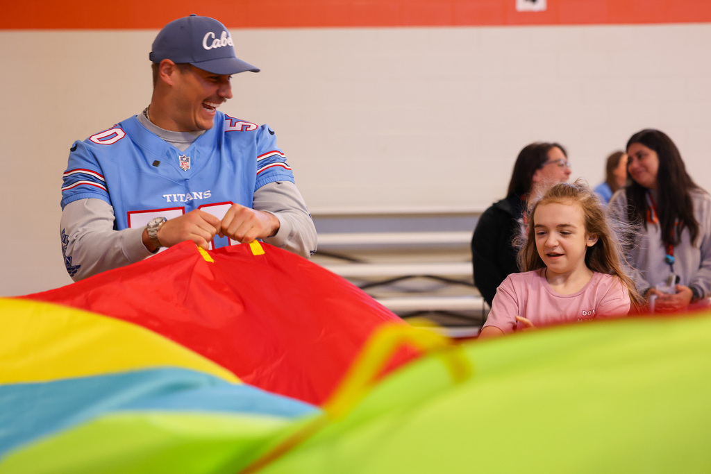 A man adjusts a red parachute as a girl looks on, with other people nearby.