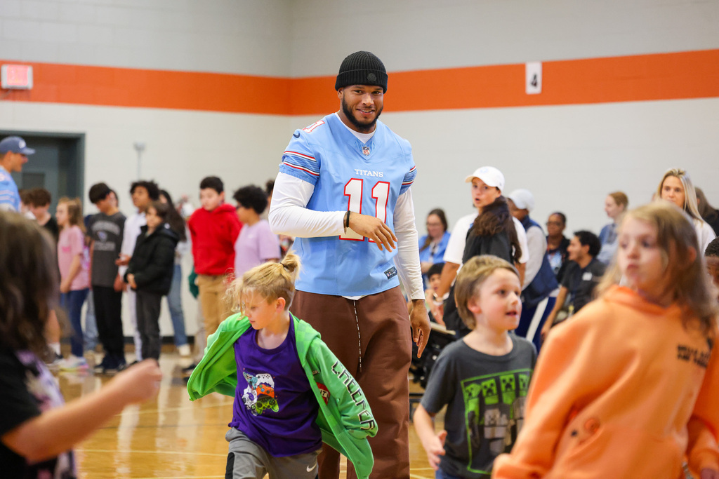 Group of students in a gymnasium. Man in sports jersey and brown pants dancing with children.