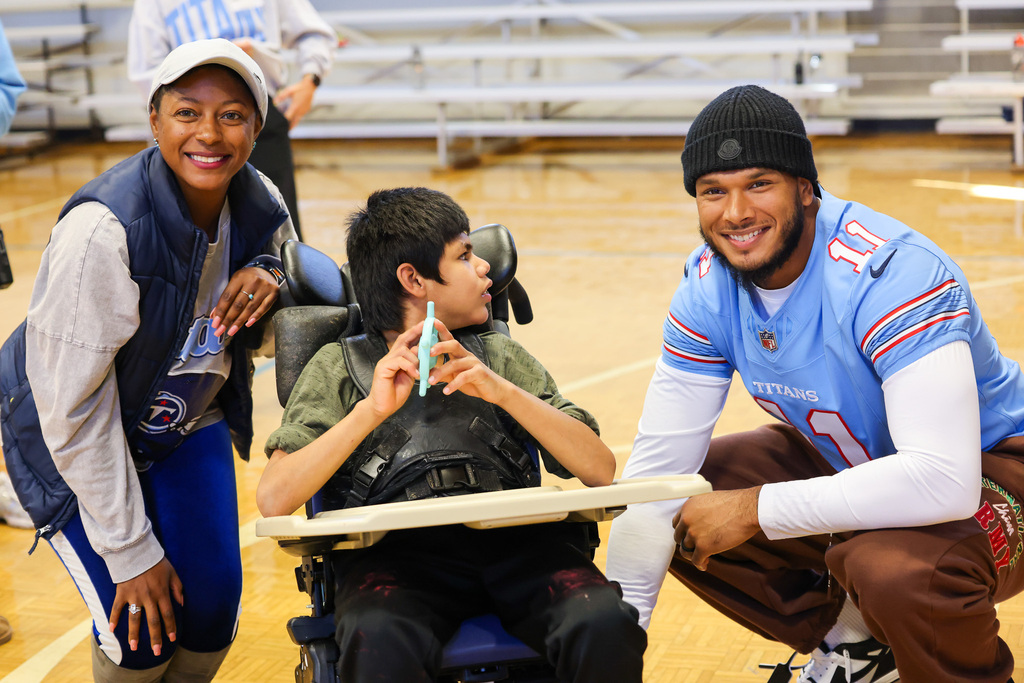 Woman, boy in wheelchair, and man in sports jersey smile, pose for photo on basketball court.