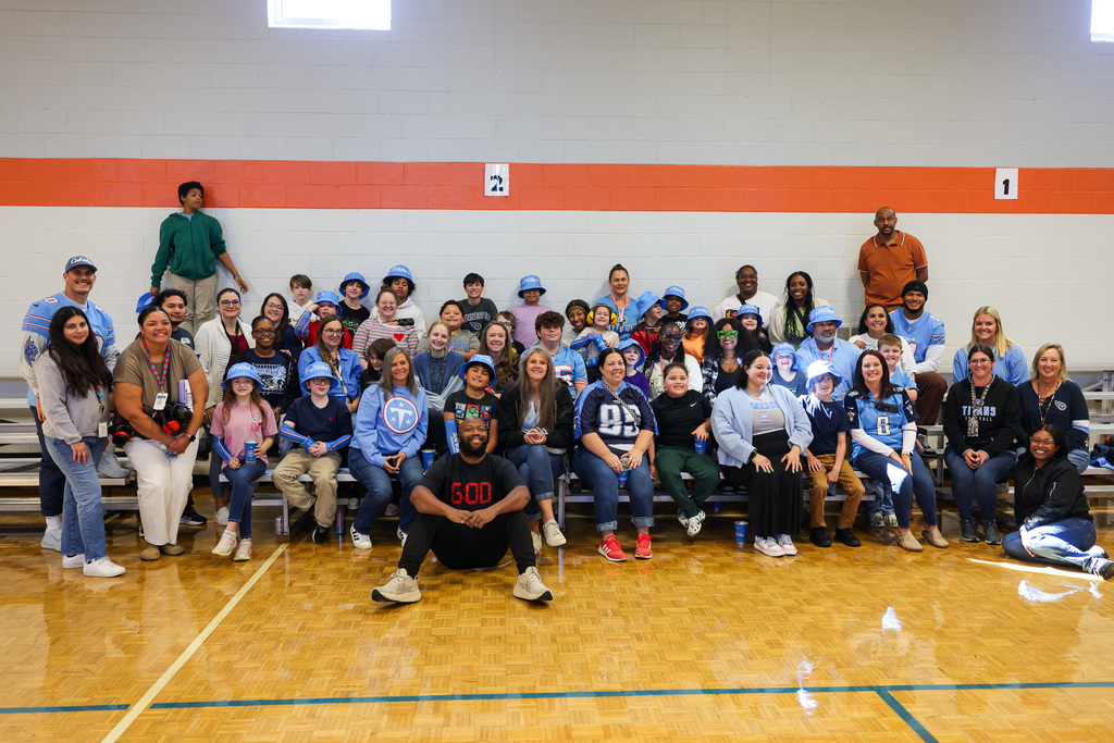 Group of people in matching shirts pose on a basketball court, some seated on bleachers.
