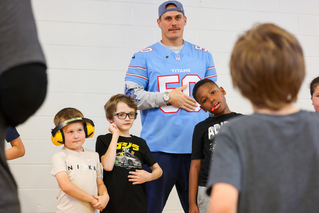 Four boys wearing ear protection stand in front of a man wearing a blue jersey.