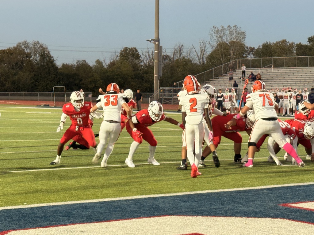 Players in red and white jerseys on a football field. Players wearing helmets and sneakers.
