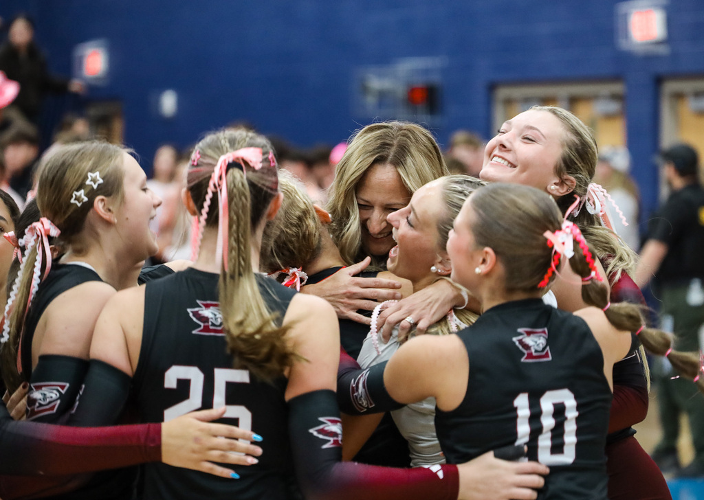 Group of girls in matching uniforms with ponytails hugging and smiling in a blue gym.
