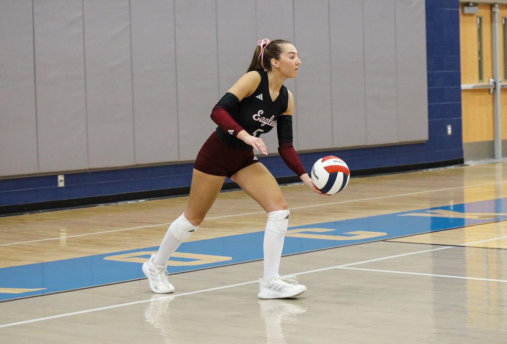 A young woman holding a volleyball practices on a court with blue markings and a wall in the background.
