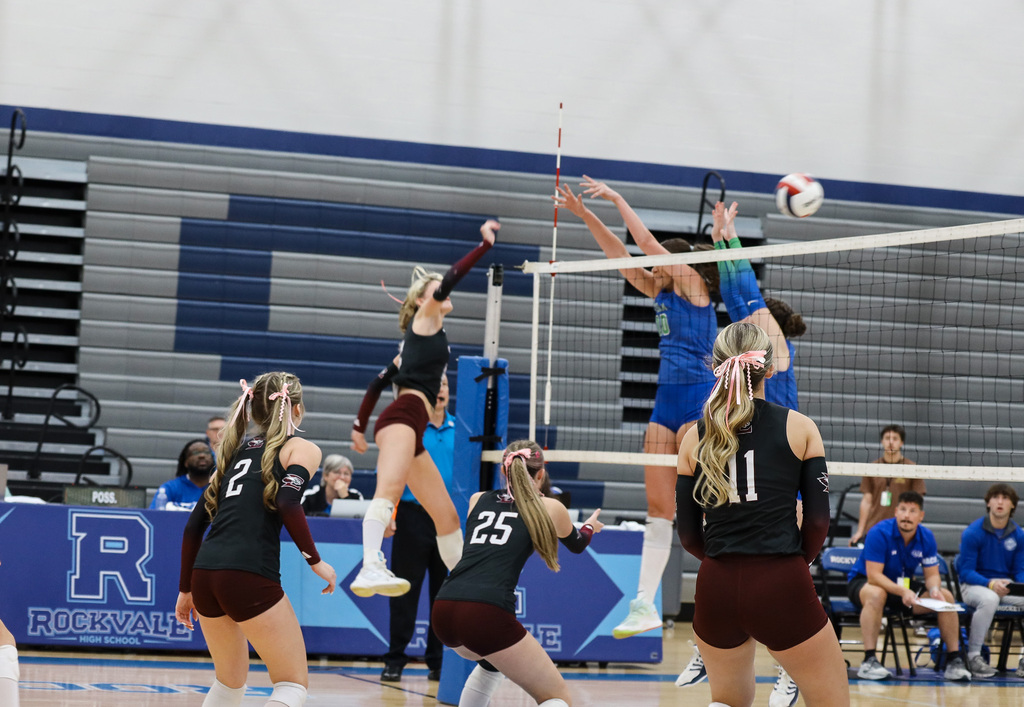A volleyball team on an indoor court. Two players are jumping to block the ball.
