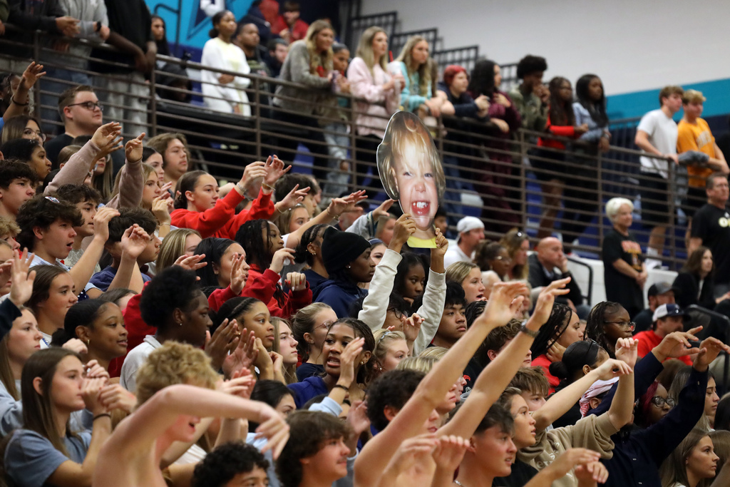 A crowd of people watching an event, some with raised arms, standing in bleachers.