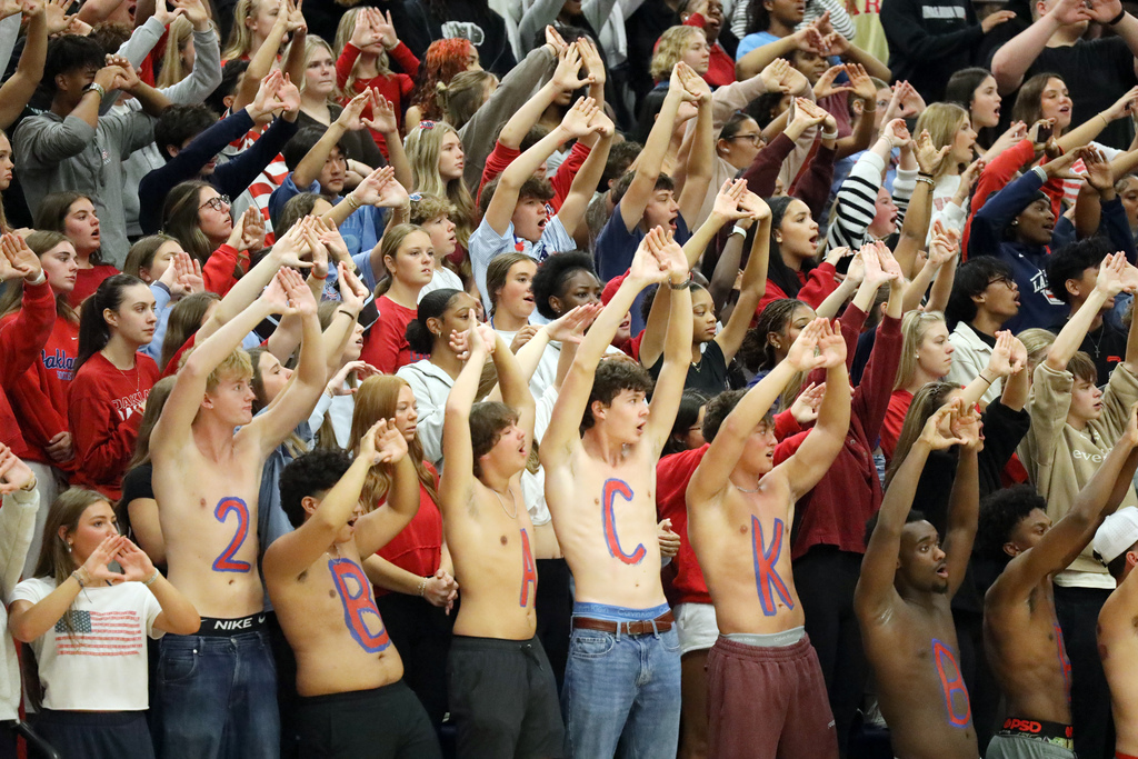 Group of young people in stands cheering, with some with paint on their chests spelling "BCK".