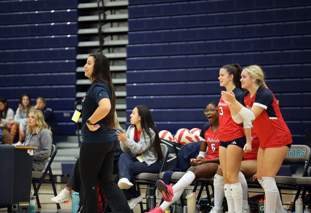 Four girls in red uniforms and white socks standing with coach on a court; bleachers in background.