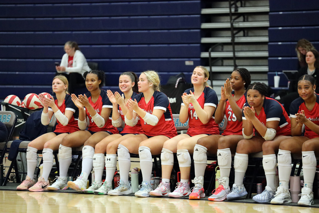 A group of women in red and blue uniforms clap while sitting in a row on a bench.