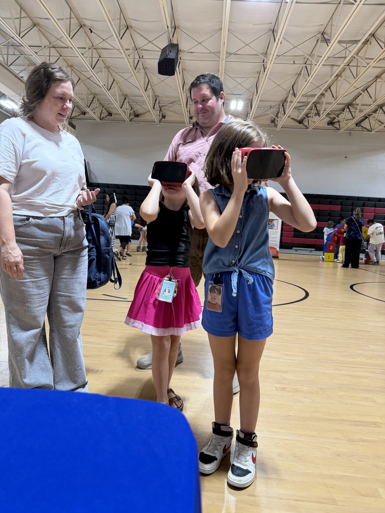 People stand in an indoor basketball court. Two young girls and a man wear virtual reality goggles.