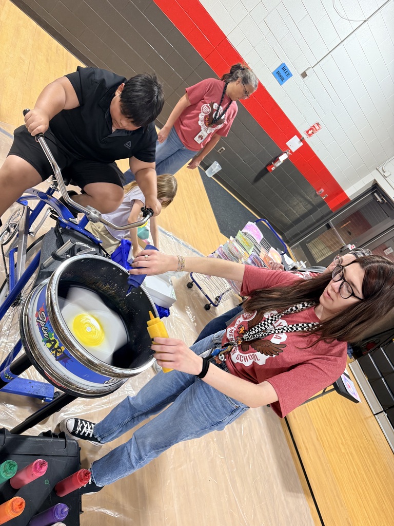 Students and adults using tools to crack eggs into a blue barrel on a wooden floor.