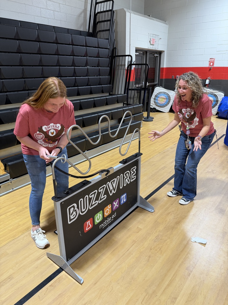 Two students standing near a standee and playing a game with a long wire.