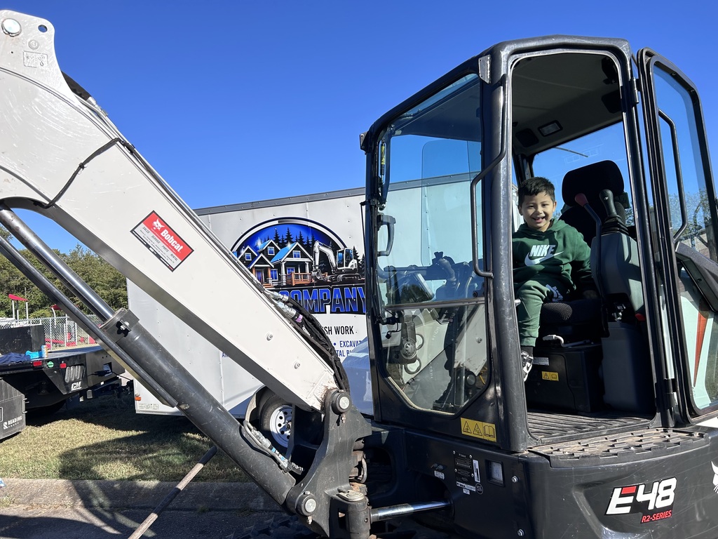 Child in green shirt sits inside cab of black and white excavator with "E48" on side.