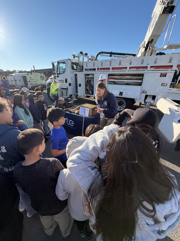 Many students gather around a table with boxes and a fire truck in the background.