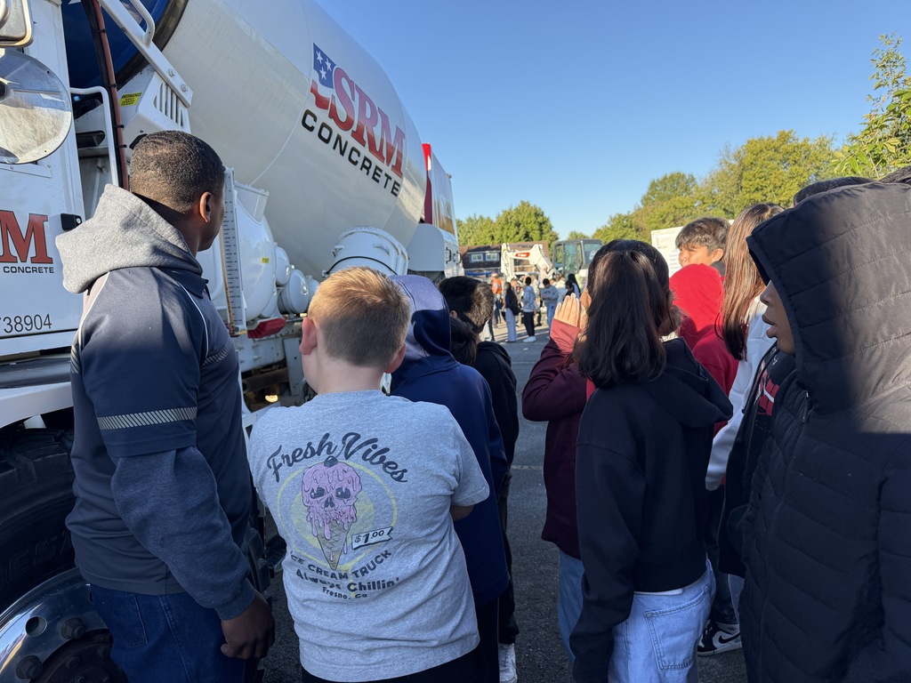 Students and adults gather around a large truck with "SDM Concrete" on its side.