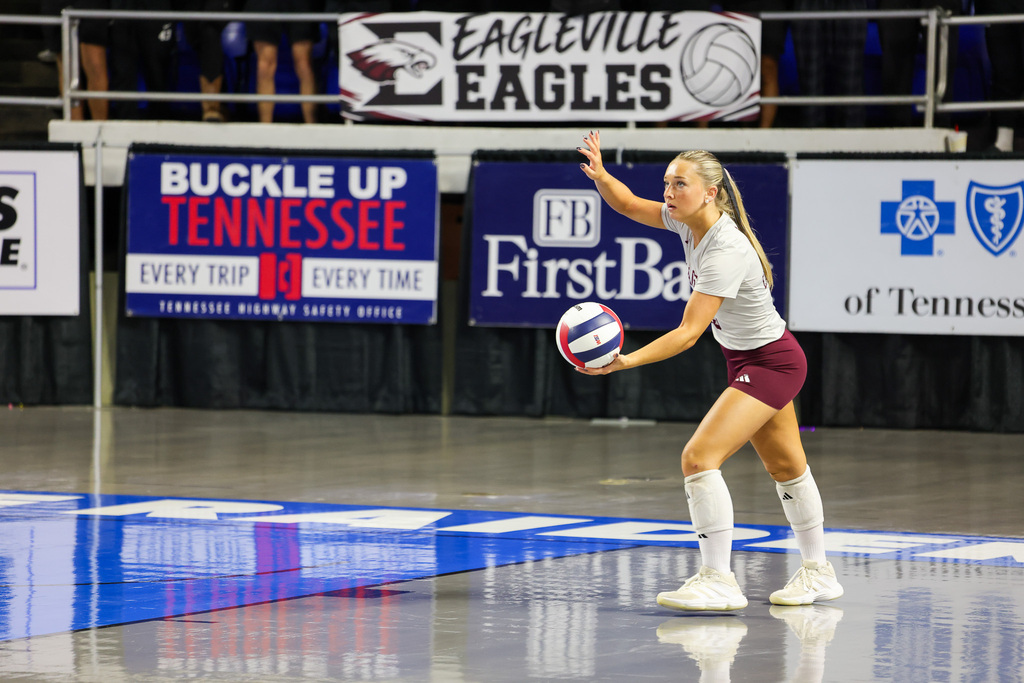 Indoor court with a woman in a white shirt and maroon shorts holding a ball.
