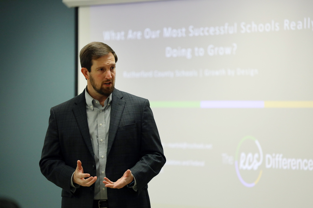 Man in a suit standing in front of a screen with a slide showing text and a logo.