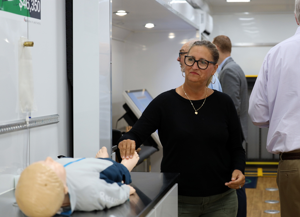 A woman wearing glasses and a necklace stands at a table next to a mannequin.