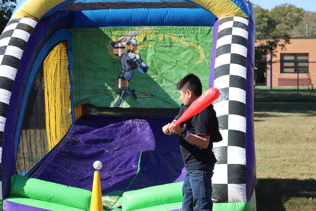 Child in a field swings red bat at a large inflatable bounce house with a castle graphic.