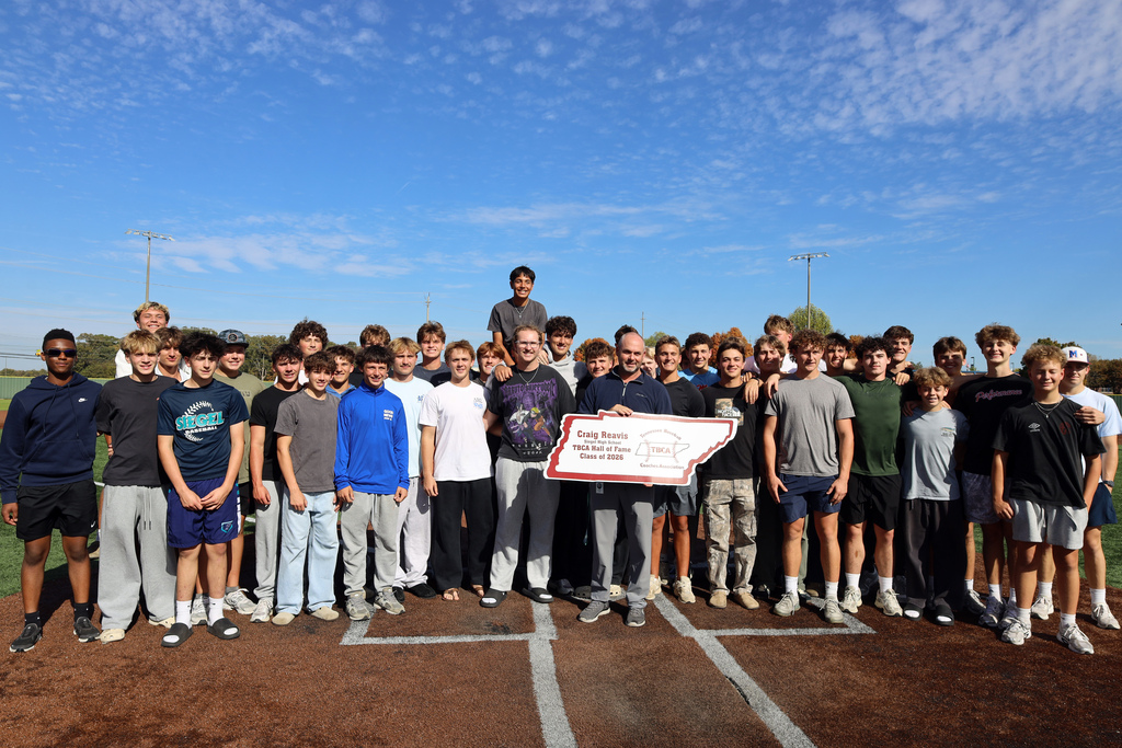 Group of people standing on a baseball field, some holding a large red and white check.