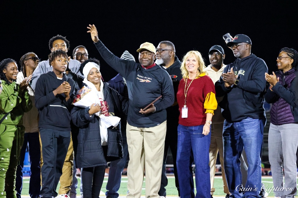 Group of people on a football field, clapping and smiling at night. Some wear winter clothing.
