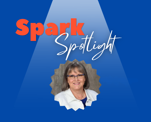 Blue background with text reading "Spark Spotlight" above a woman in a white coat, glasses, and necklace.