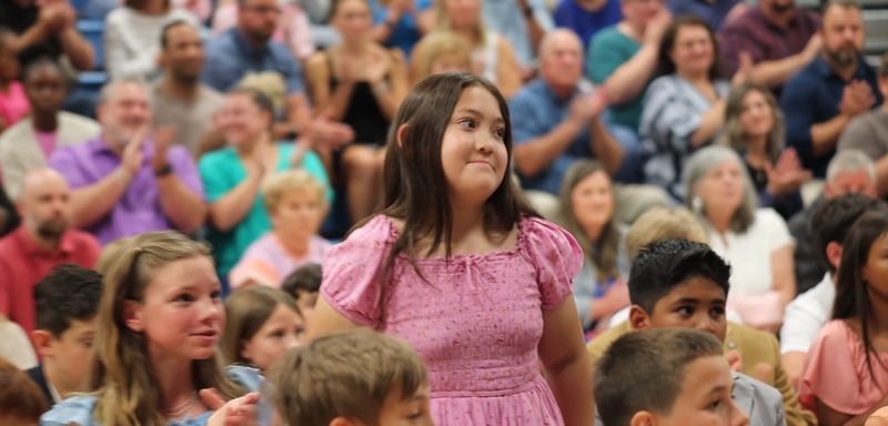 Girl in pink dress stands to be recogized as audience applauds