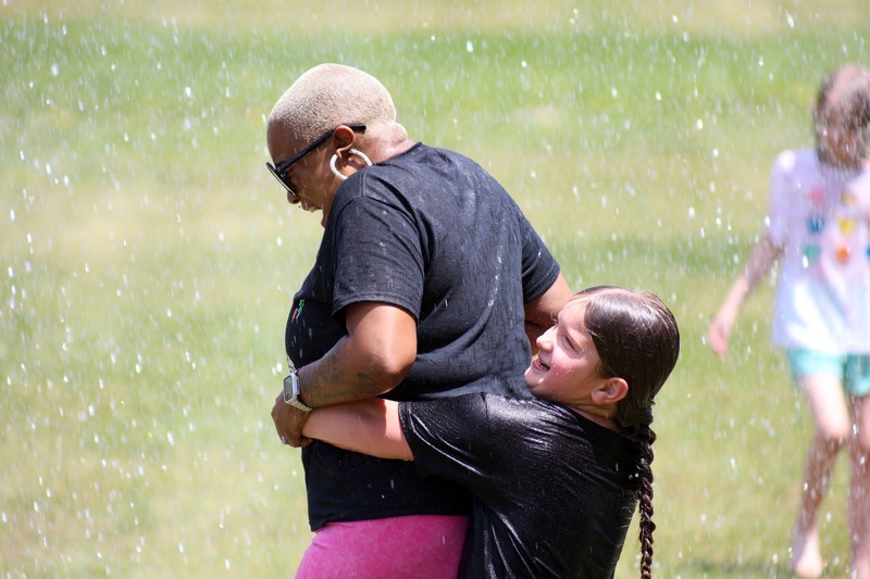 student in black shirt hugs teacher in black shirt in sprinklers