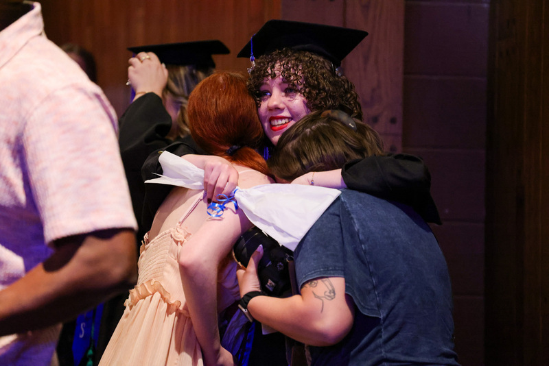 Student in cap and gown hugs supporters