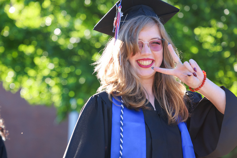 Student in cap and gown flashes peace sign