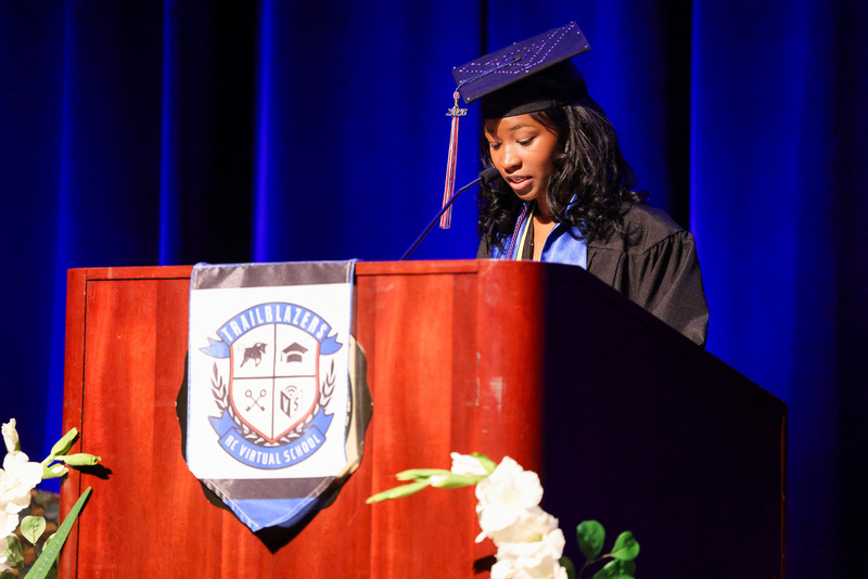 Student in cap and gown speaks at podium