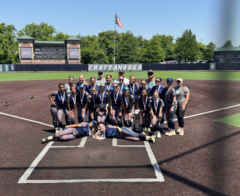 softball team holding championship trophy near home plate