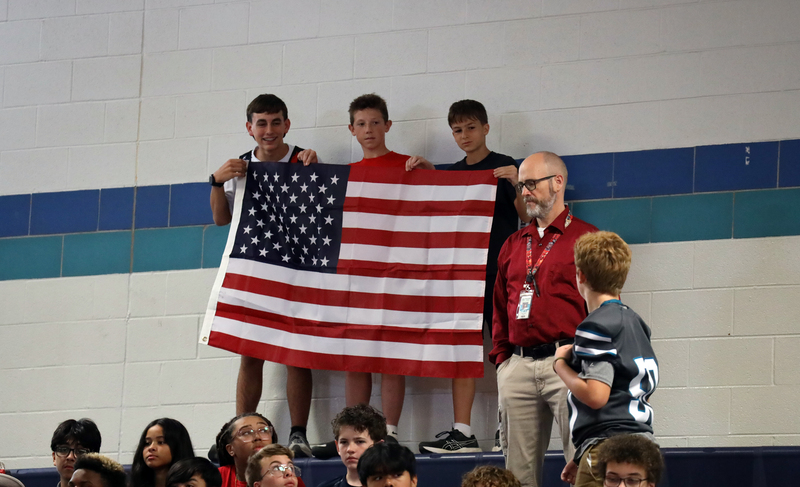 three boys hold american flag in school gym
