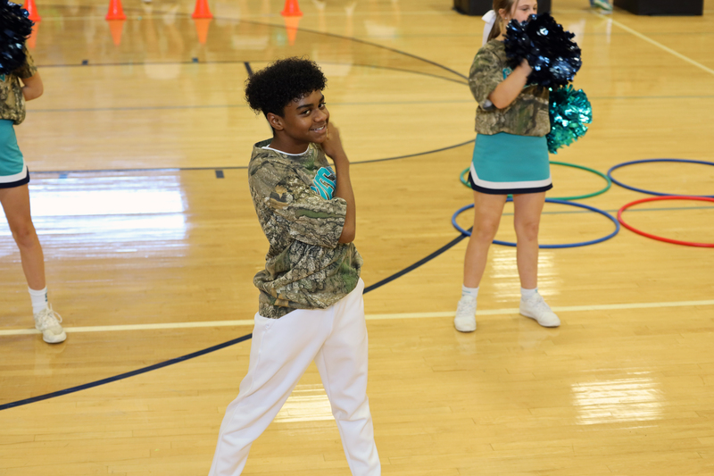 boy in camo shirt and white pants dances at pep rally