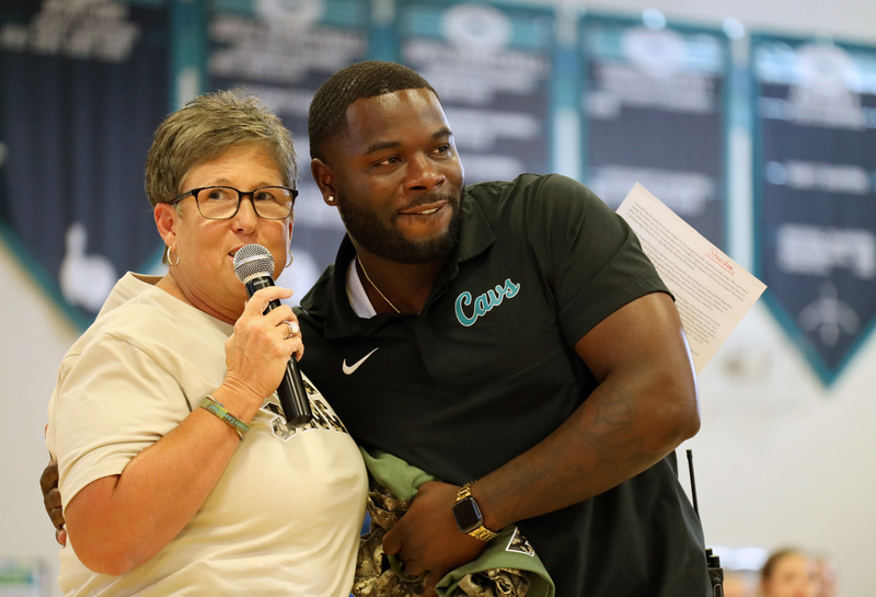 woman with short hair holds microphone and hugs male teacher in black shirt