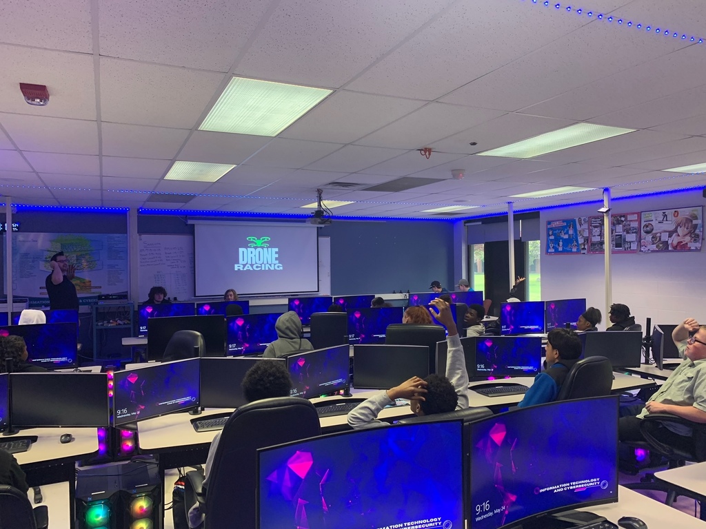 Students behind computers with a teacher in the front of the room and "Drone Racing" on the screen
