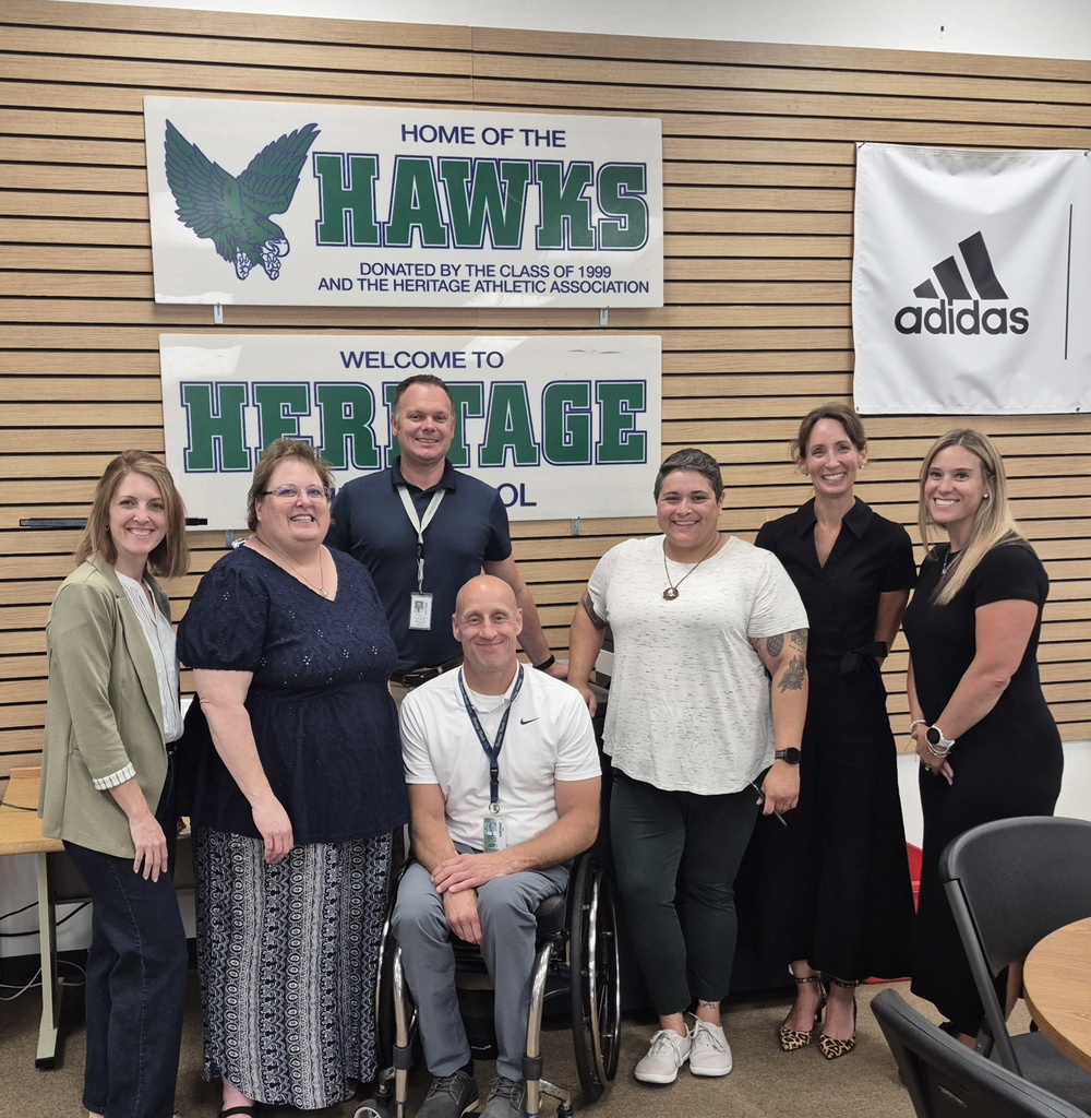 A group of educators who presented the day's professional learning stand in front of a Heritage High School banner