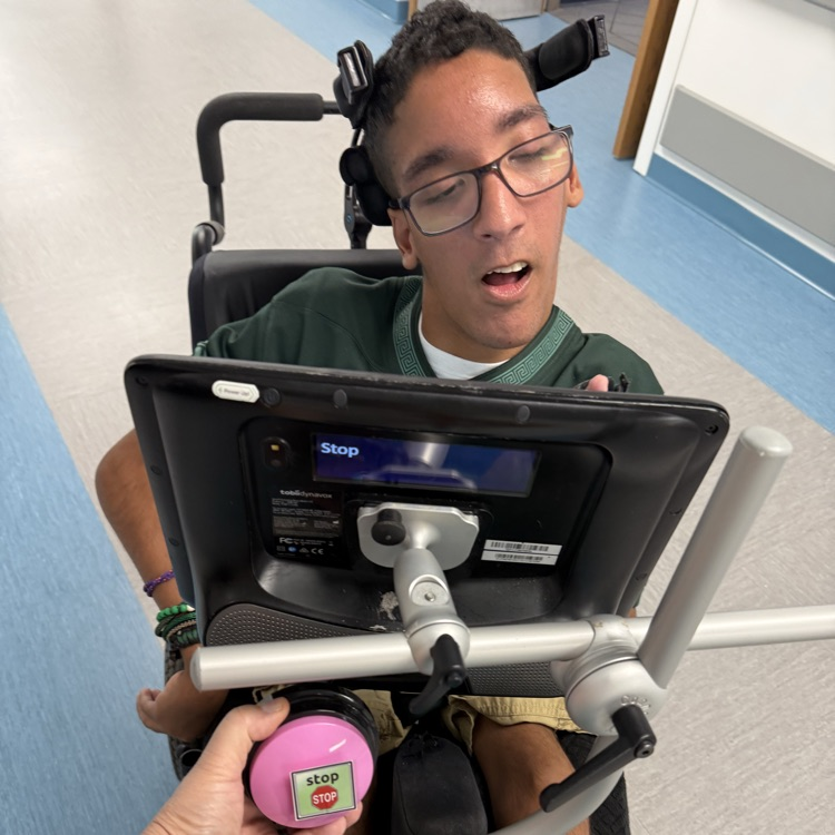 young adult male wheelchair user student speaking through a speech device to record the word STOP on a speech button  