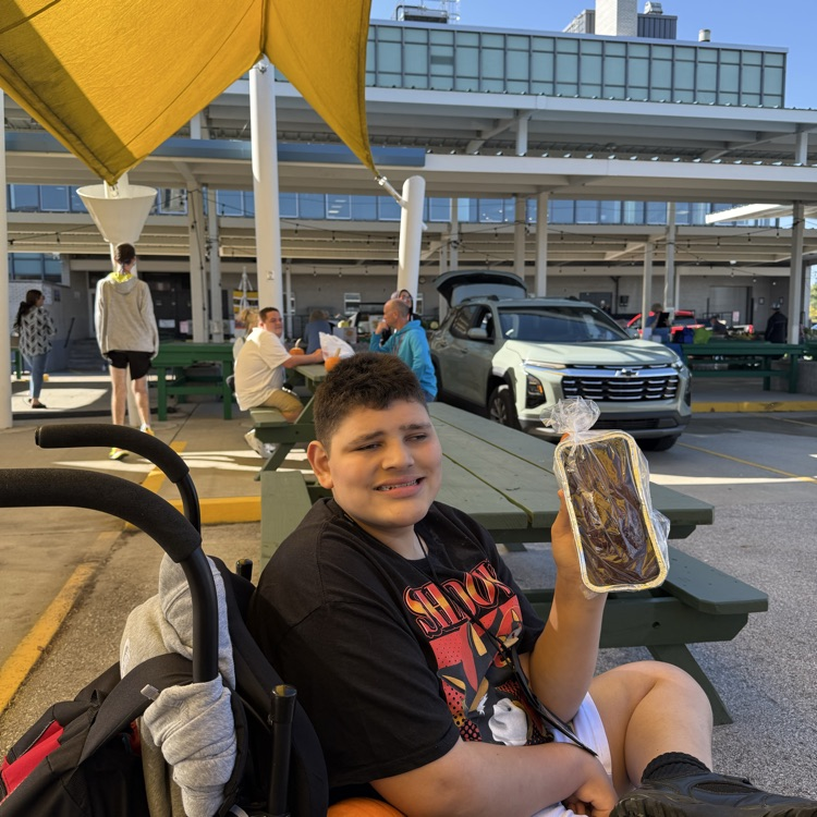 adult male wheelchair user holding up a loaf of banana bread at an outdoor farmers market on a sunny day