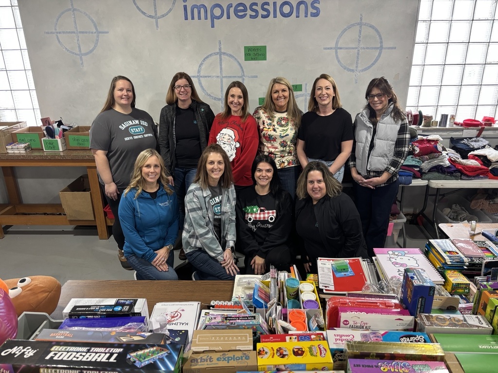 A group of Saginaw ISD staff pose for a photo in front of tables of clothing and toy donations for the City Rescue Mission