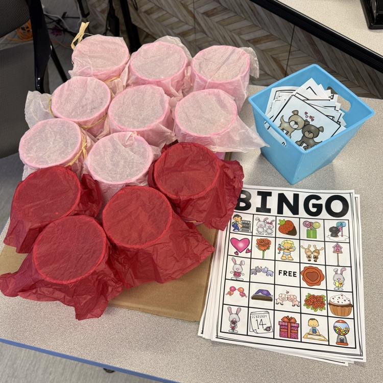 Printed valentine picture bingo cards on a table next to a homemade prize board and a bin of bingo calling cards