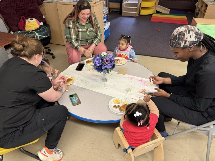 3 women sitting at a round table with 3 toddlers eating lunch 
