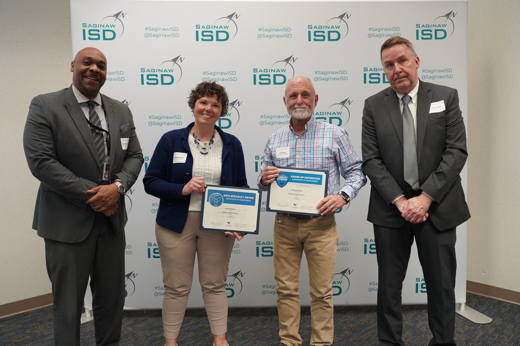 Four people pose for a photo while holding certificates. Two men and one woman wear formal suits, and one man wears a blue shirt.