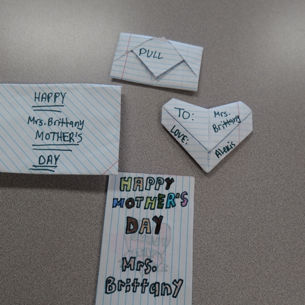 Four handmade greeting cards on a gray surface. Cards feature blue lines, white envelopes, and "Happy Mother's Day" messages.