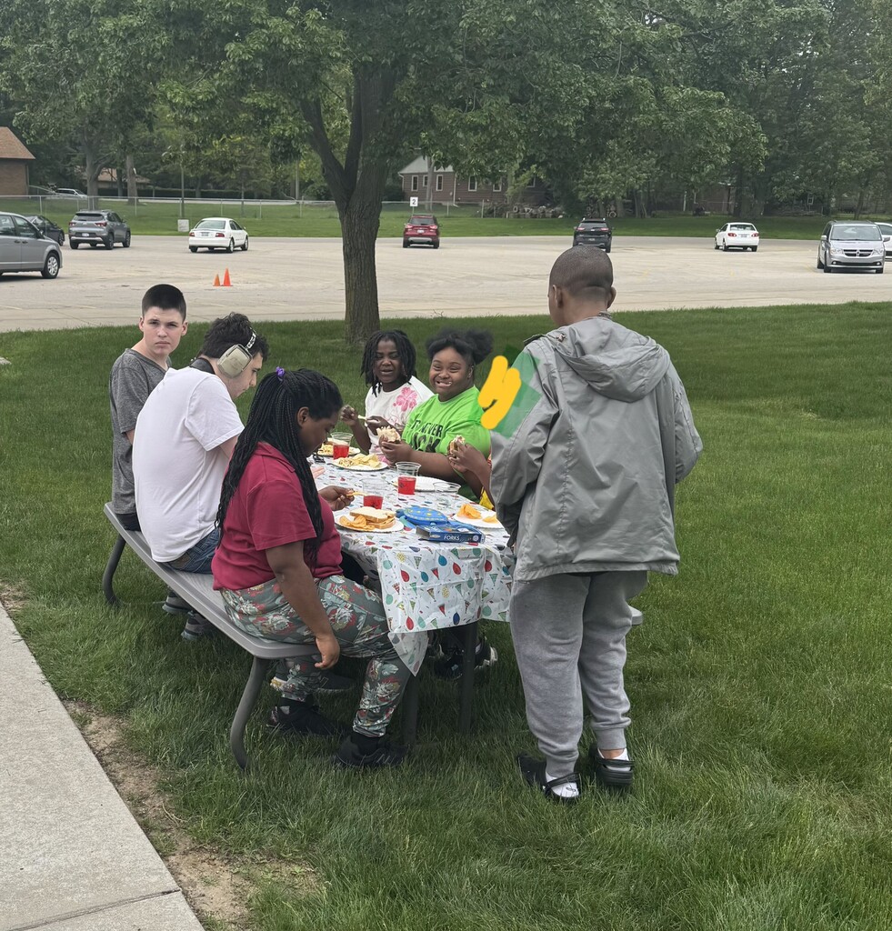 students outside at a picnic table in the grass eating a picnic lunch together