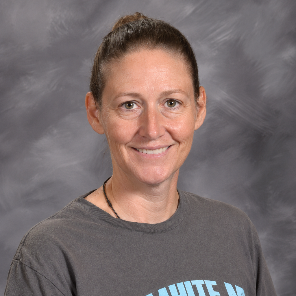 A woman with short hair smiles for a photo. She wears a grey t-shirt with blue text on the front.