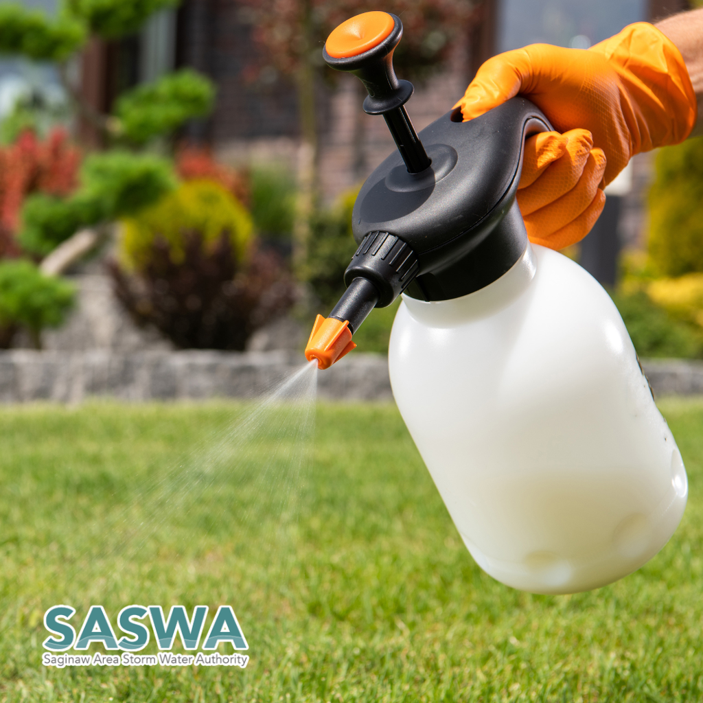 A person in orange gloves spraying water on a green lawn. A white bottle with black and orange handles.