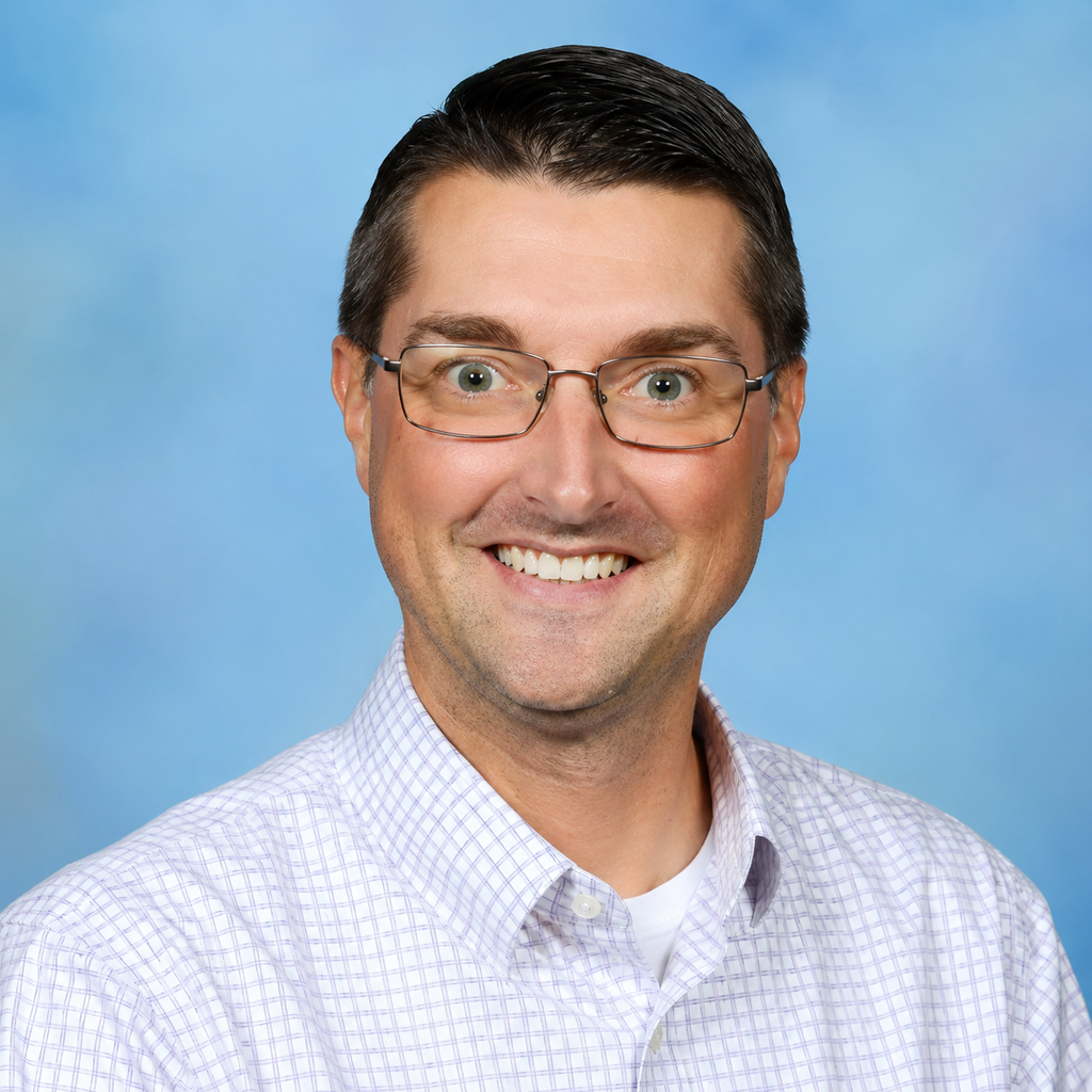 A man wearing glasses smiles at the camera, standing in front of a blue gradient background.