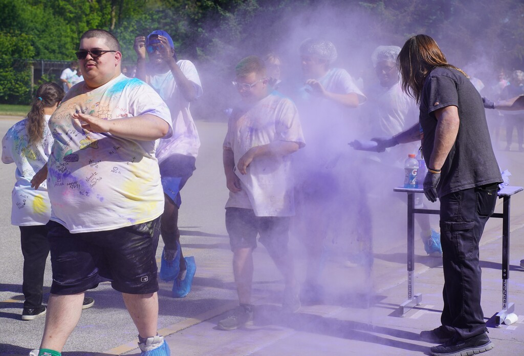 A group of people at an event with purple powder in the air, wearing shirts and shorts.
