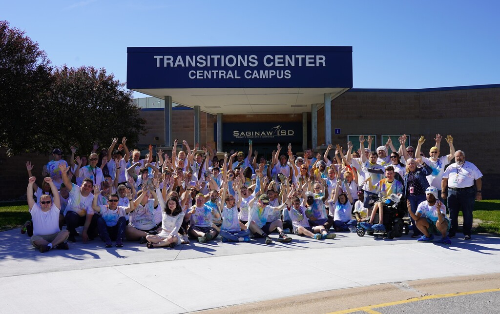 A group of people wearing white shirts poses for a photo in front of a Transitions Center Central Campus building.